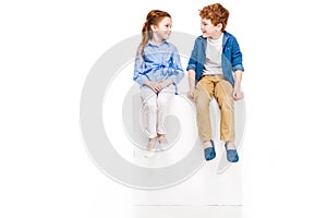 adorable little children sitting on white cube and smiling each other