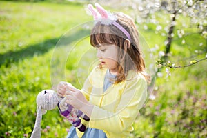 Adorable little funny bunny girl holding rabbit toy in the spring blossom garden