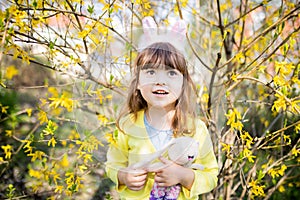 Adorable little funny bunny girl holding rabbit toy in the spring blossom garden