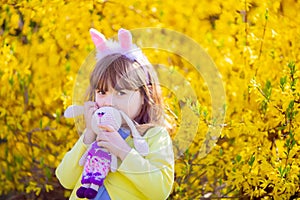 Adorable little funny bunny girl holding rabbit toy in the spring blossom garden