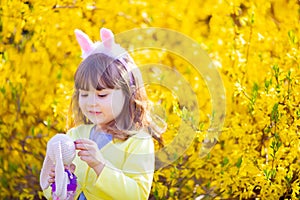 Adorable little funny bunny girl holding rabbit toy in the spring blossom garden