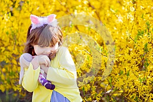 Adorable little funny bunny girl holding rabbit toy in the spring blossom garden