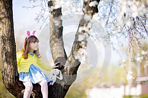 Adorable little funny bunny girl sitting at the blooming three at sunny spring day