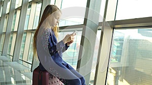 Adorable little girl in airport near big window indoor playing with smartphone
