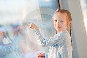 Adorable little girl in airport near big window looking at big aircraft