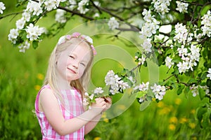 Adorable little girl in blooming apple tree garden on beautiful spring day