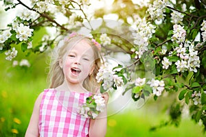 Adorable little girl in blooming apple tree garden on beautiful spring day