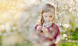 Adorable little girl in blooming cherry tree garden on beautiful spring day