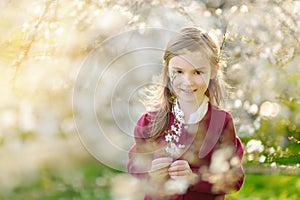 Adorable little girl in blooming cherry tree garden on beautiful spring day