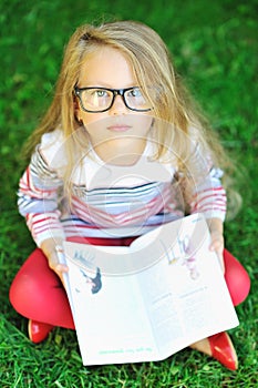 Adorable little girl with a book wearing glasses - outdoors