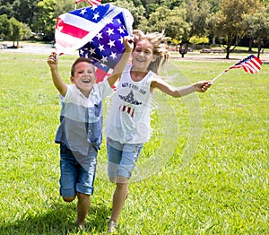 Adorable little girl and boy run on bright green grass holding american flag outdoors on Independence Day holiday