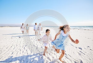 Adorable little girl and boy running together on sandy beach while parents follow in the background. Carefree sibling