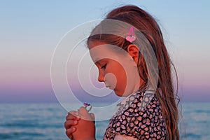 Adorable little girl child looks at the flower on beach. Portrait of a child with wet long hair in dress sniffing flower