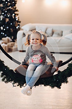 Adorable little girl on Christmas swing. Christmas tree.