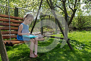 Adorable little girl is concentrated on learning to write while sitting on a swing on a sunny day