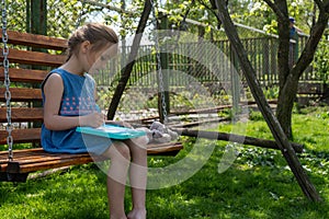 Adorable little girl is concentrated on learning to write while sitting on a swing on a sunny day