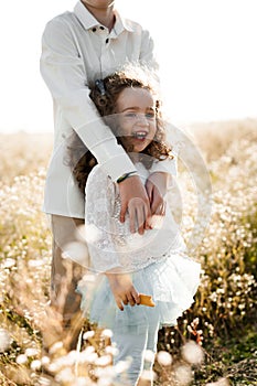 Adorable little girl with curly hair laughing in the arms of her older brother