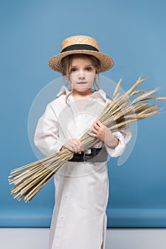 adorable little girl in dress and straw boater holding wheat ears and looking