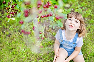 Adorable little girl eating cherry from cherry-tree in the orchard