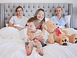 Adorable little girl embracing her younger brother with her teddybear next to her while sitting on a bed with per