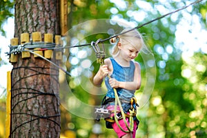 Adorable little girl enjoying her time in climbing adventure park on warm and sunny summer day