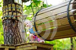 Adorable little girl enjoying her time in climbing adventure park on warm and sunny summer day