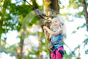 Adorable little girl enjoying her time in climbing adventure park on warm and sunny summer day