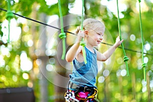 Adorable little girl enjoying her time in climbing adventure park on warm and sunny summer day