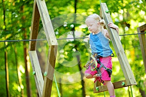 Adorable little girl enjoying her time in climbing adventure park on warm and sunny summer day