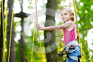 Adorable little girl enjoying her time in climbing adventure park on warm and sunny summer day