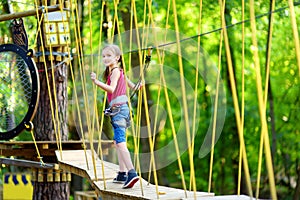 Adorable little girl enjoying her time in climbing adventure park on warm and sunny summer day