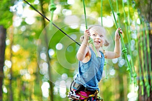 Adorable little girl enjoying her time in climbing adventure park on warm and sunny summer day