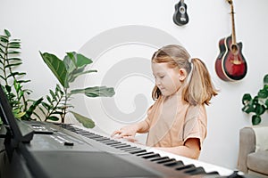 Adorable little girl enjoys playing electric piano at home. Side view.