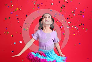 Adorable little girl and falling confetti on red background