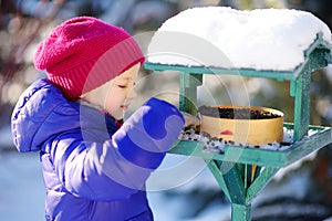 Adorable little girl feeding birds on chilly winter day in city park. Child helping birds at winter.