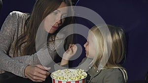 Adorable little girl feeding her mom with popcorn at the cinema