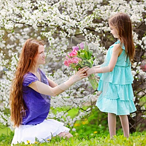 Adorable little girl handing tulips to her mother in blooming cherry garden