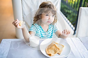 Adorable little girl having breakfast, eating pancakes and drinking milk