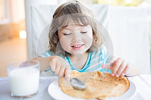 Adorable little girl having breakfast, eating pancakes and drinking milk