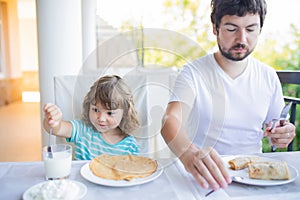 Adorable little girl having breakfast with her father, eating pancakes and drinking milk