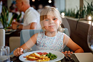 Adorable little girl having breakfast at resort restaurant. Happy preschool child eating healthy food, vegetables and