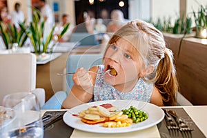 Adorable little girl having breakfast at resort restaurant. Happy preschool child eating healthy food, vegetables and