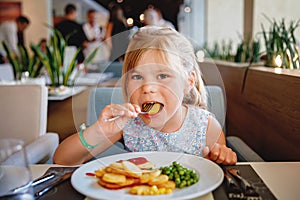 Adorable little girl having breakfast at resort restaurant. Happy preschool child eating healthy food, vegetables and