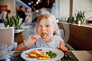 Adorable little girl having breakfast at resort restaurant. Happy preschool child eating healthy food, vegetables and