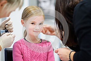 Adorable little girl having ear piercing process in beauty center