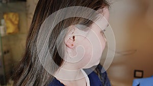 Adorable little girl having ear piercing process with special equipment in beauty center by medical worker