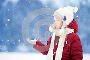 Adorable little girl having fun in beautiful winter park. Cute child playing in a snow.