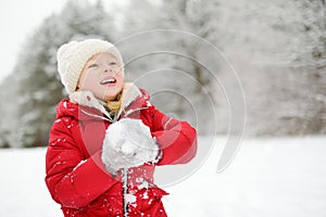 Adorable little girl having fun in beautiful winter park. Cute child playing in a snow.