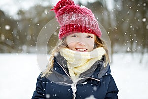 Adorable little girl having fun in beautiful winter park. Cute child playing in a snow.