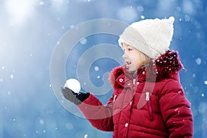 Adorable little girl having fun in beautiful winter park. Cute child playing in a snow.